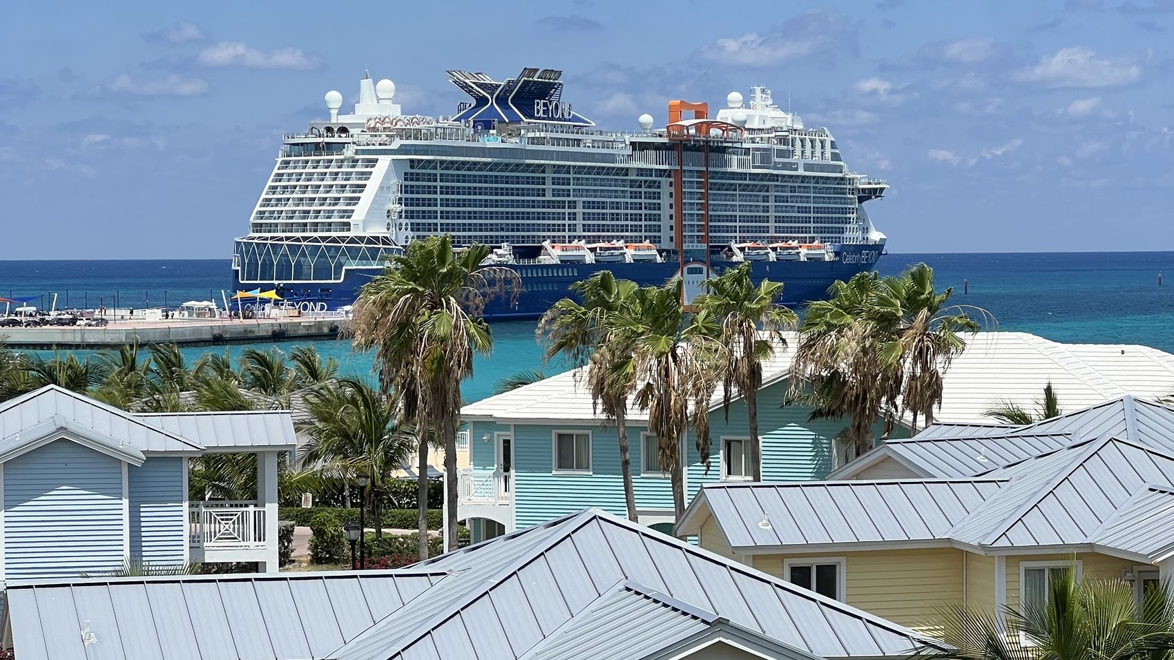 Celebrity Beyond at anchor beyond pastel island rooftops and palm trees
