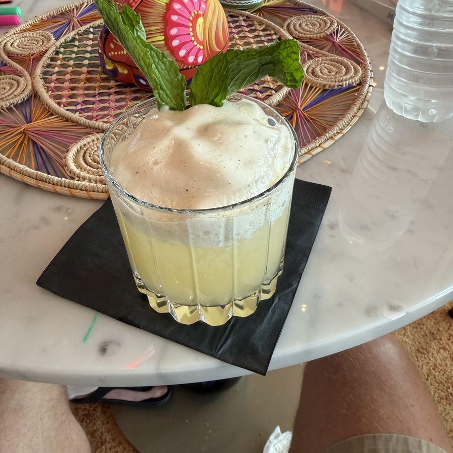 A cocktail garnished with mint on a marble table beside hand-painted Mexican folk art