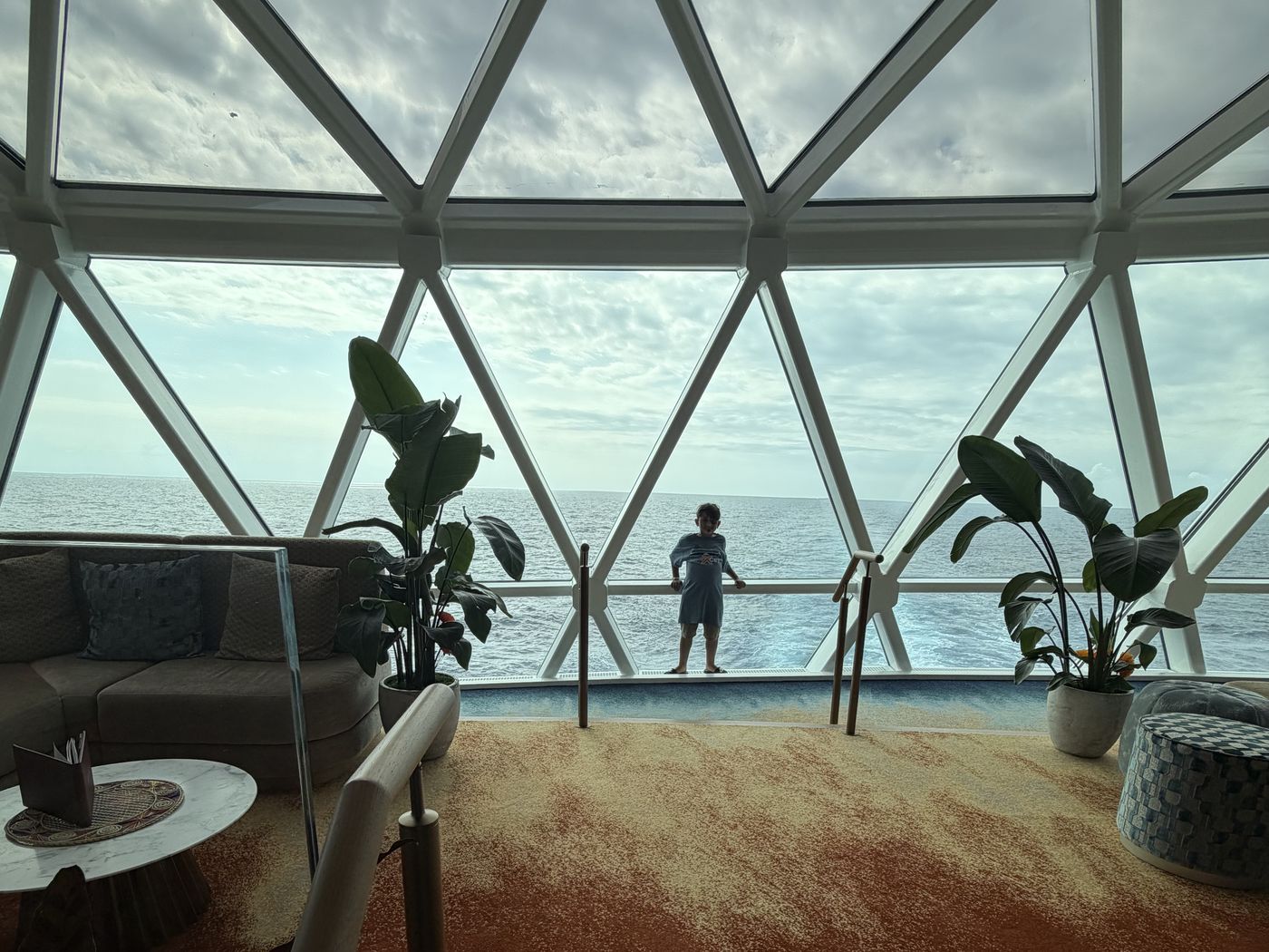 A triangulated glass dome at the stern of the ship framing the open ocean and the wake