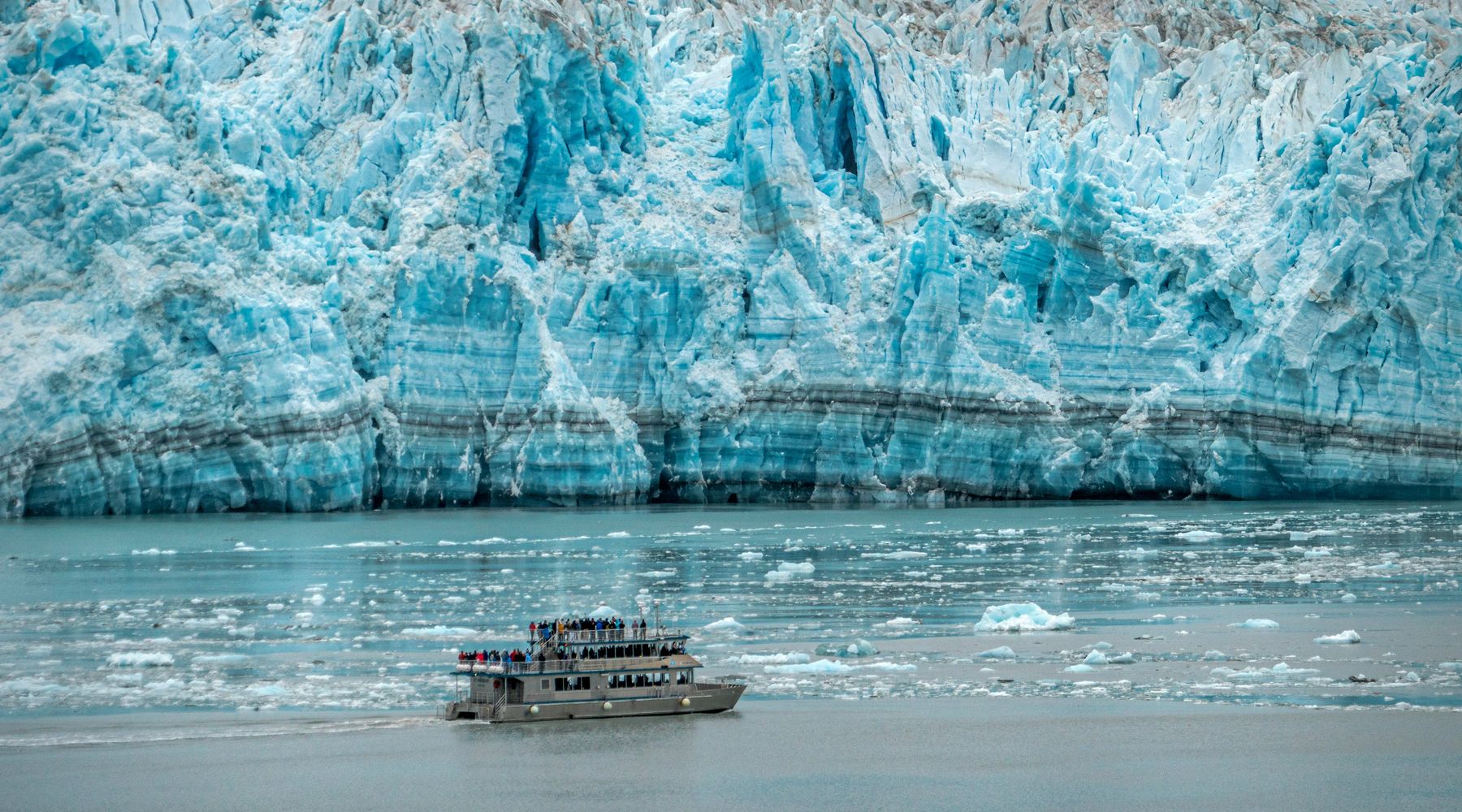 A tour boat dwarfed by the towering blue face of an Alaskan tidewater glacier