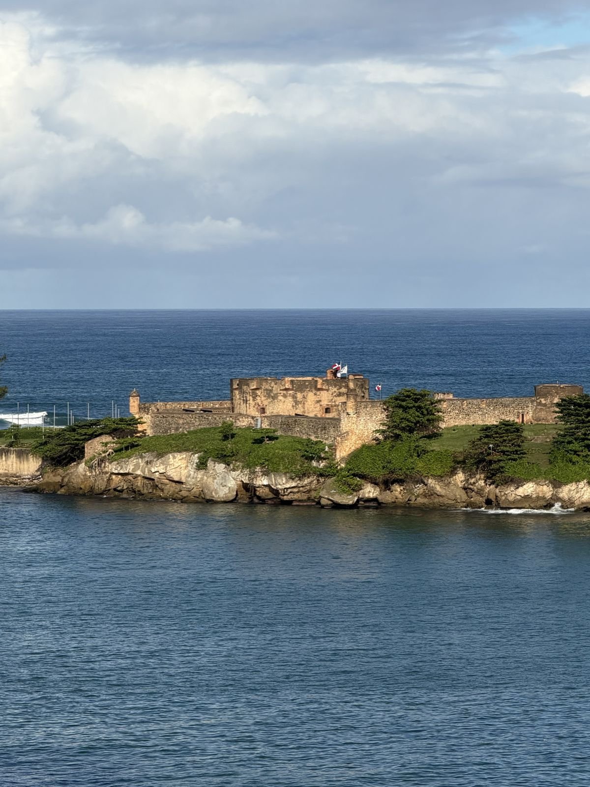 An old stone fort on a green headland above the sea, seen from a ship