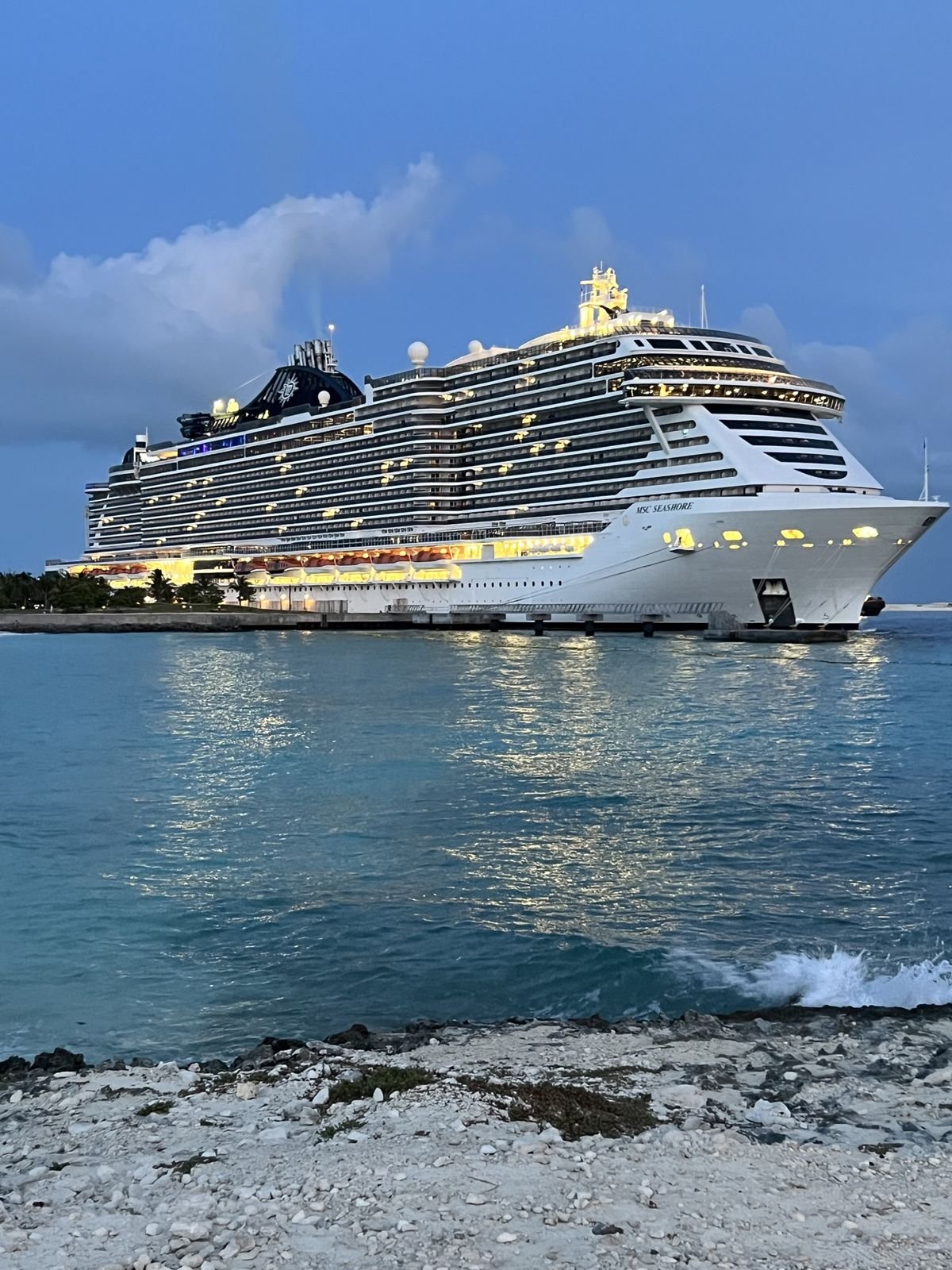 A cruise ship docked at dusk with its lights reflected in the water