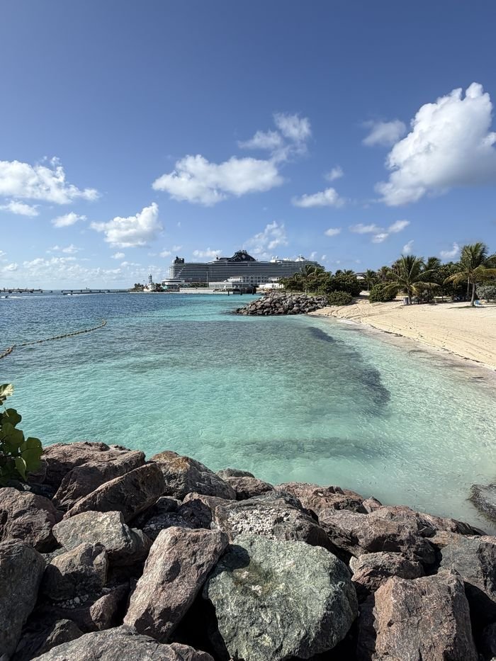 Clear turquoise water and a sandy beach at Ocean Cay, with MSC Seashore docked at the pier in the distance.