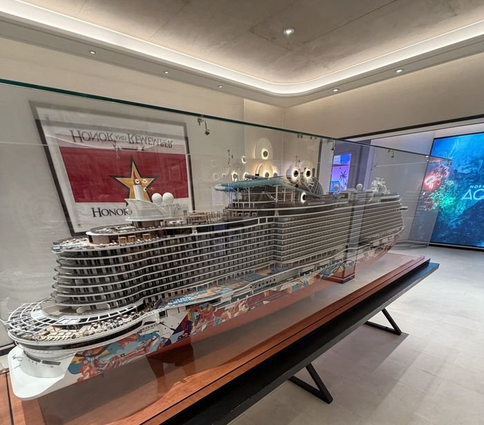 The bow of the Norwegian Aqua scale model seen up close through its glass case, showing the stacked forward balconies and the curved top decks.