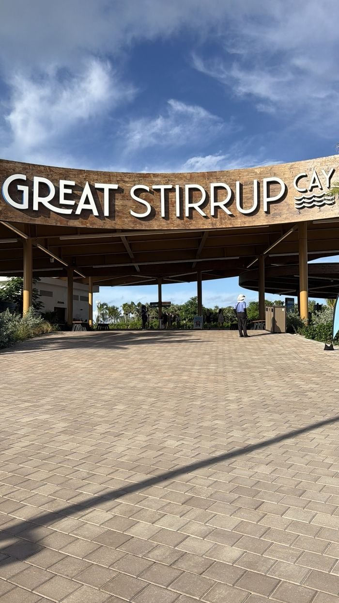 A curved wooden welcome canopy reading Great Stirrup Cay over a wide paved plaza, under a deep blue sky.