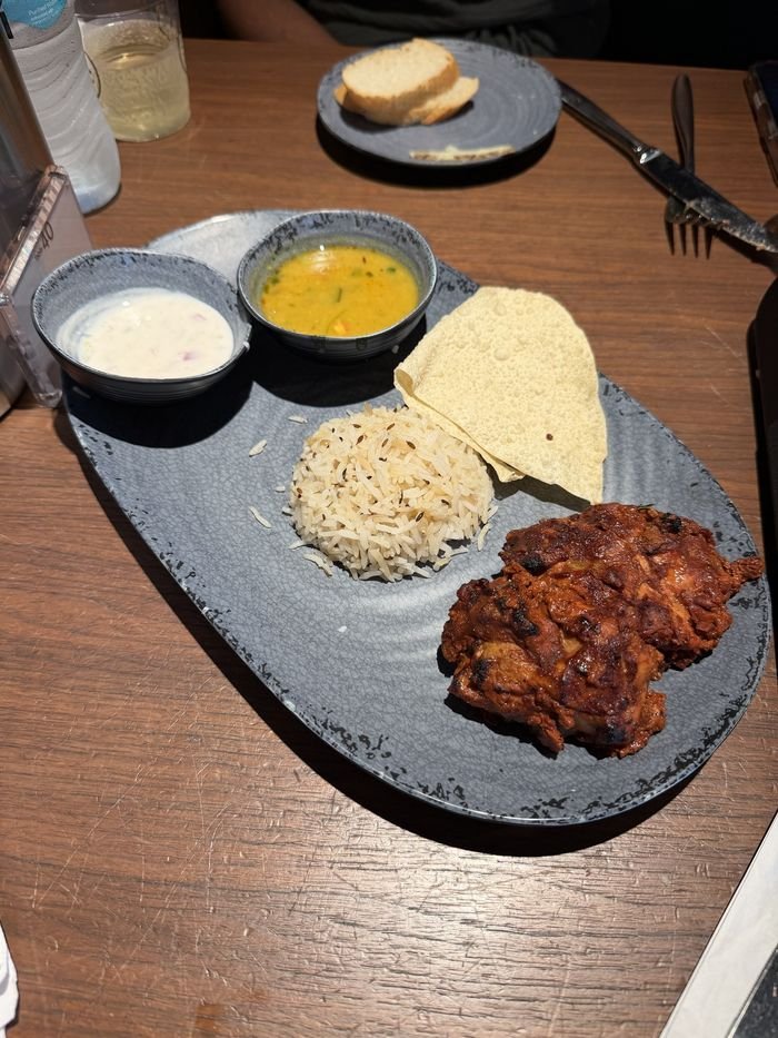 A plate of tandoori-style chicken, cumin rice and a papadum, with small bowls of dal and raita.