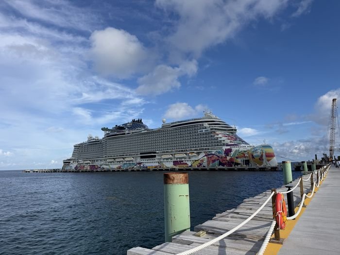 Norwegian Aqua, her hull painted in a colorful mural, docked at the pier at Great Stirrup Cay under a blue sky with scattered clouds.