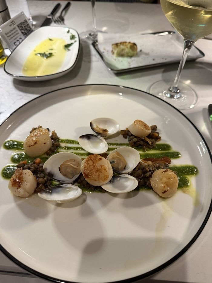 Seared scallops and clams in their shells on lentils with a bright green herb sauce, on a white plate.