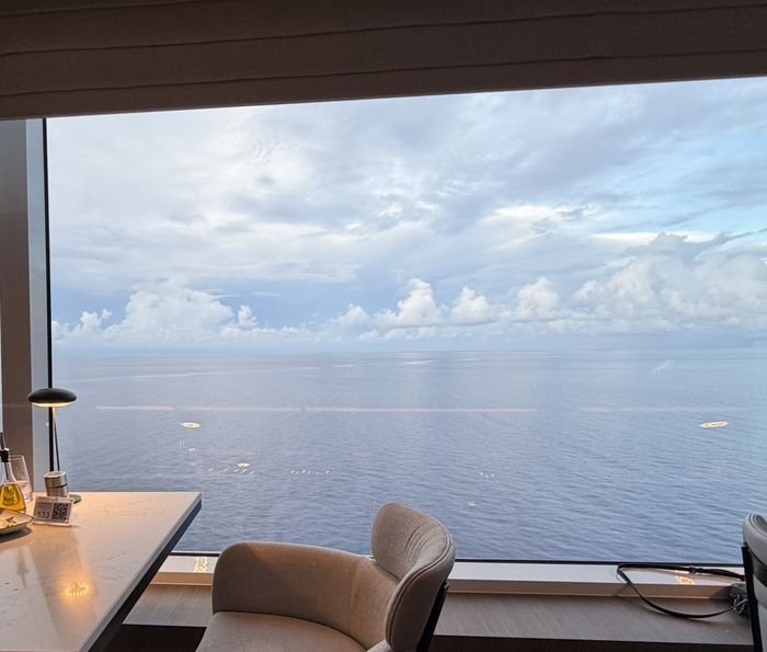A table set beside a floor-to-ceiling window in Palomar on Norwegian Aqua, looking out over calm open ocean under scattered clouds.
