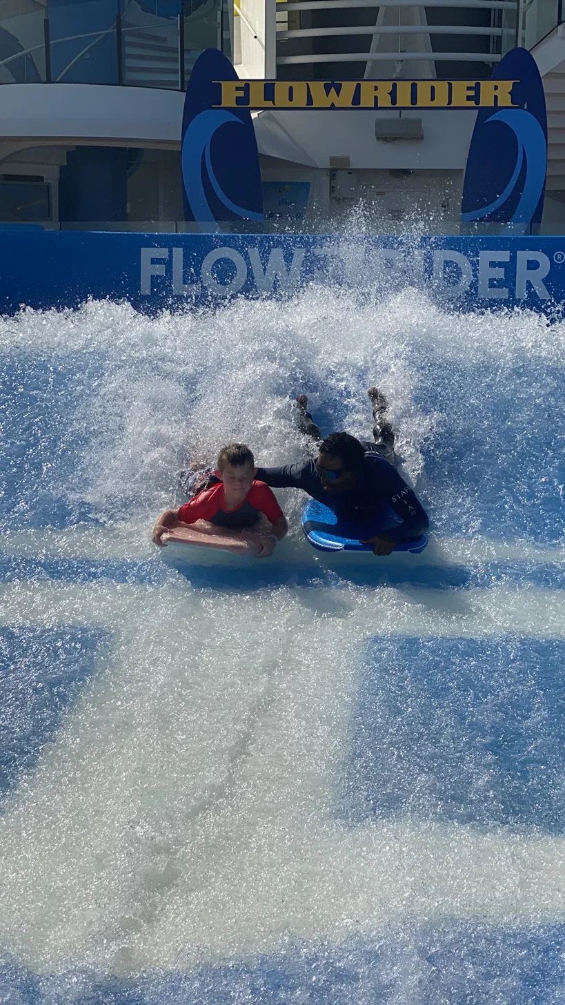 An instructor helping Jaxon ride the FlowRider on a Royal Caribbean cruise ship.