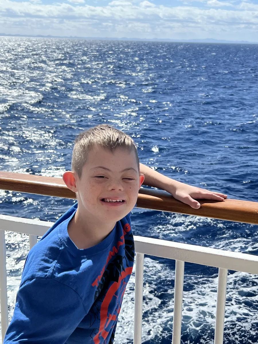 Jaxon, who has Down syndrome, smiling on a cruise ship railing looking at the ocean