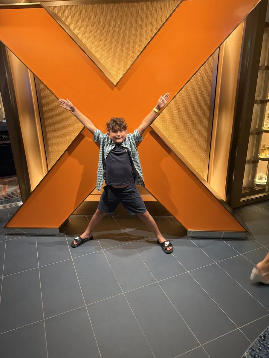A boy posing in front of a large orange X sign aboard Celebrity Xcel
