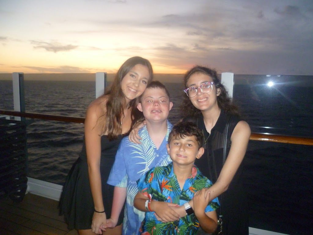 Four children standing together on a cruise ship deck at sunset.
